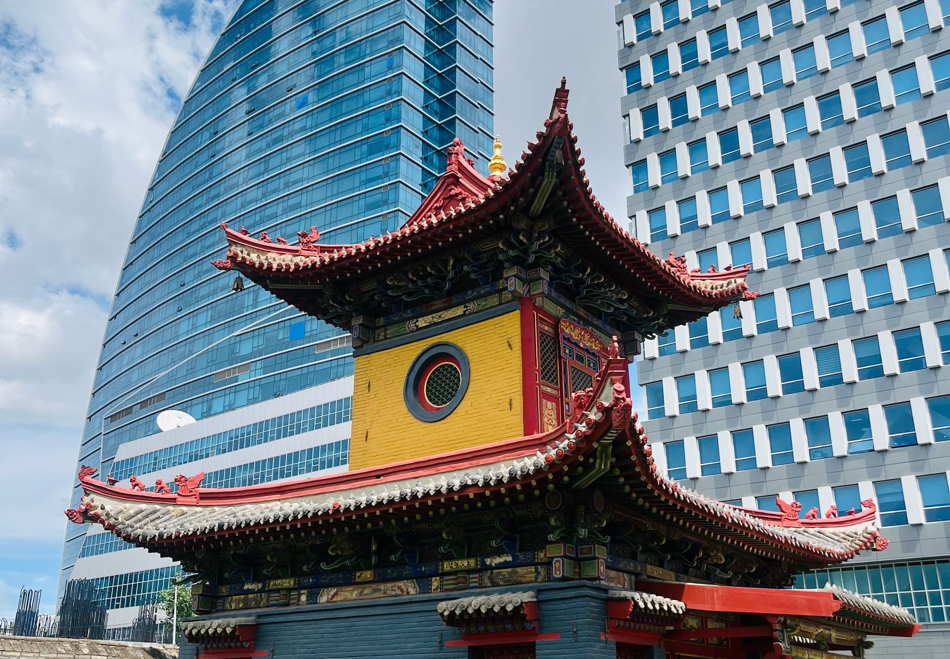 Colorful Buddhist temple building in Ulaanbaatar, Mongolia, framed by modern glass and office towers under a blue sky.